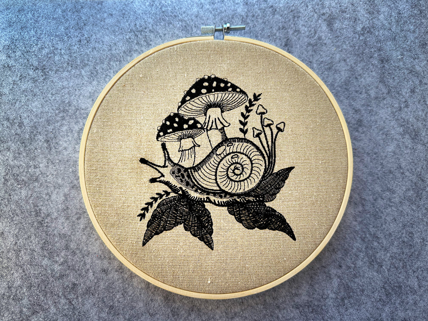 Snail and mushroom embroidery pattern stitched on linen in a hoop