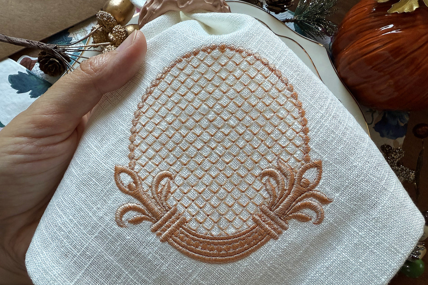 Embroidered design on a white fabric held by a hand, with a blurred natural background.