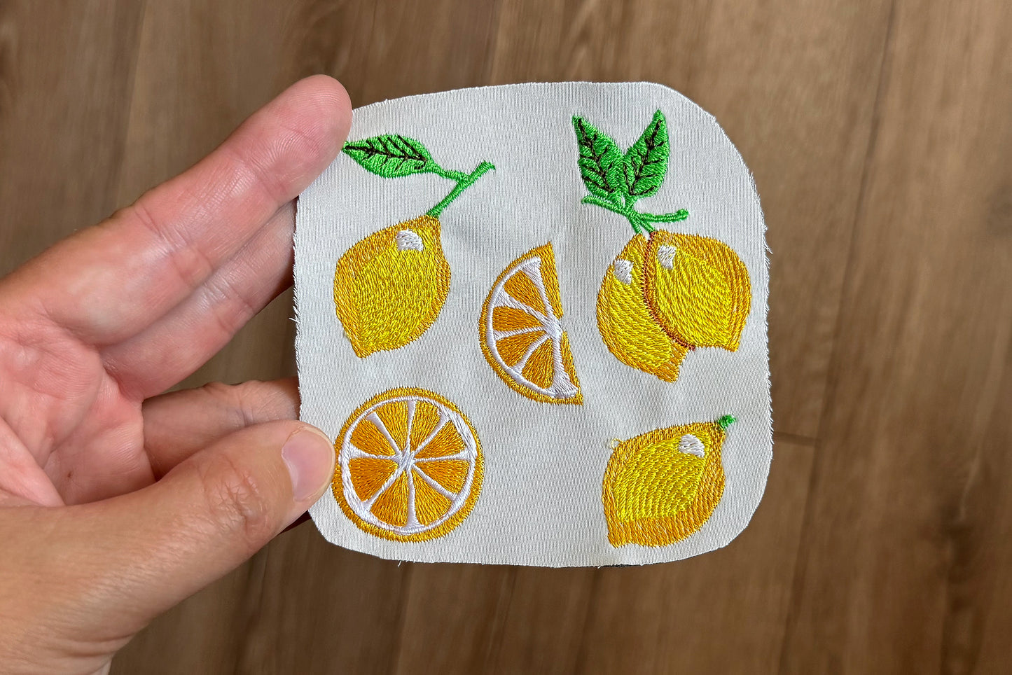 Embroidered patch with lemons and oranges held by a hand on a wooden background