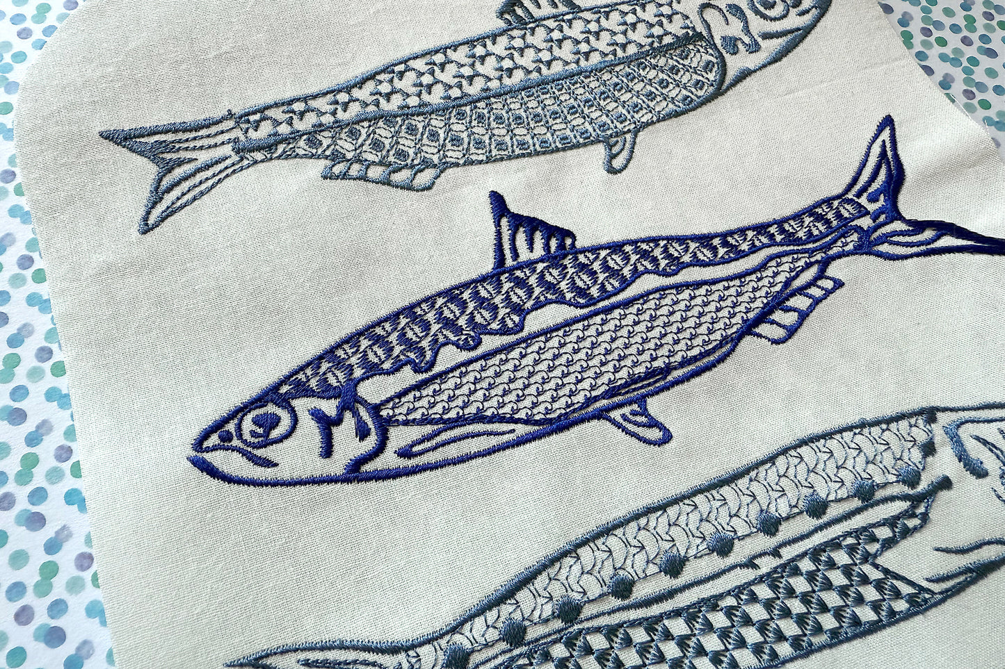 Embroidered fish design on a white fabric background with blue thread.