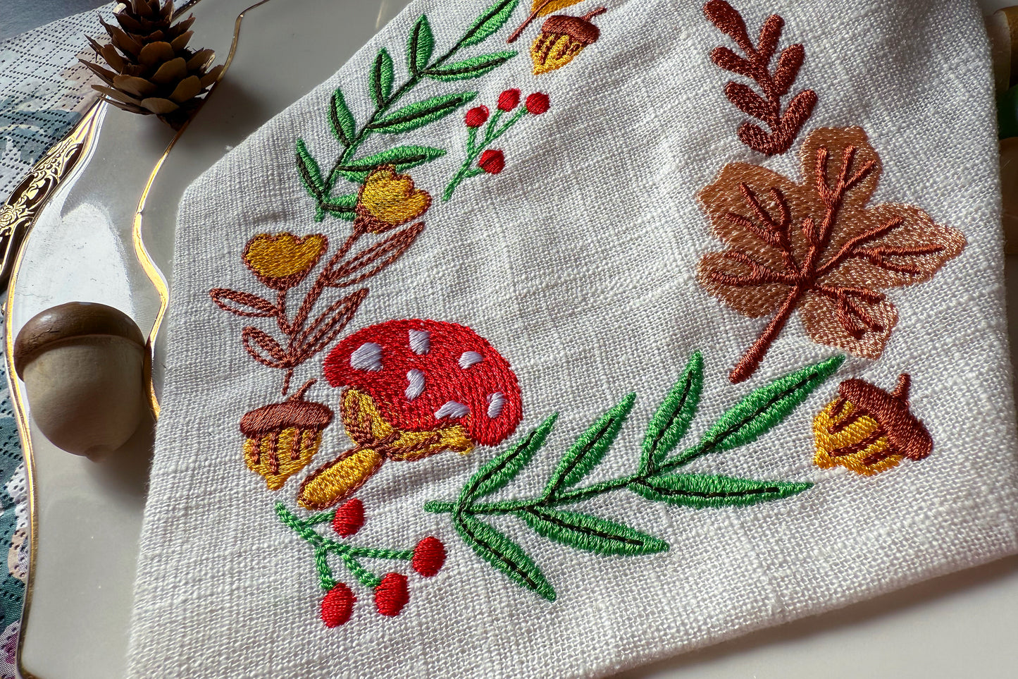 Embroidered fabric with autumn-themed design featuring leaves, acorns, and berries on a white background.