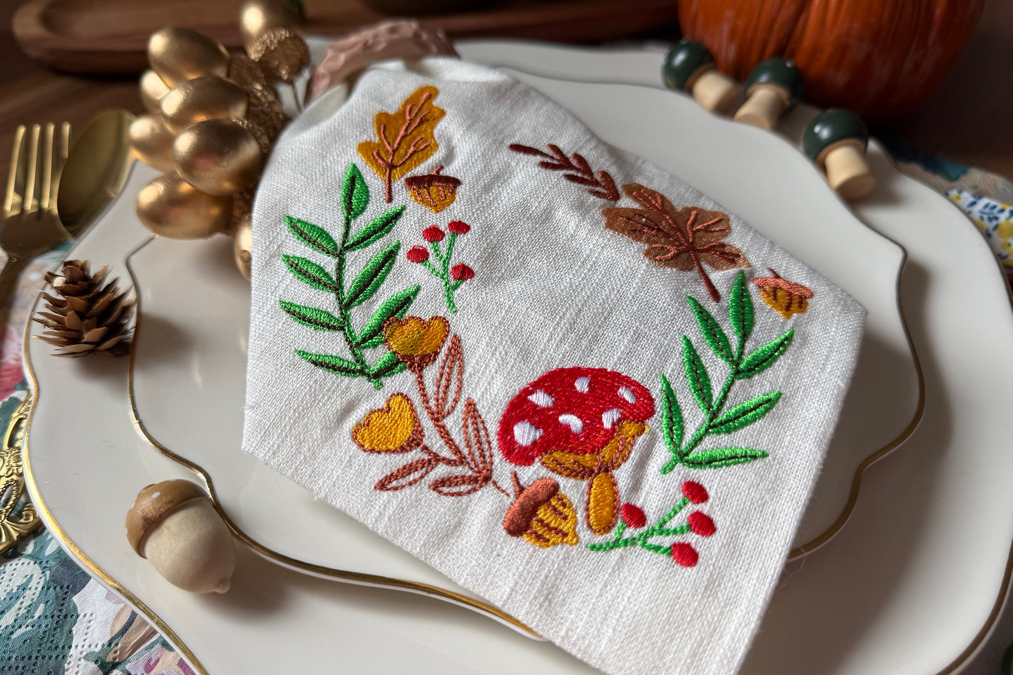 Embroidered napkin with autumn design on a decorative plate with pumpkins and acorns.