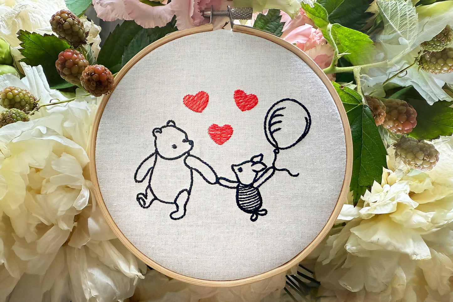 Finished Winnie and Piglet embroidery displayed in wooden hoop on soft brown background