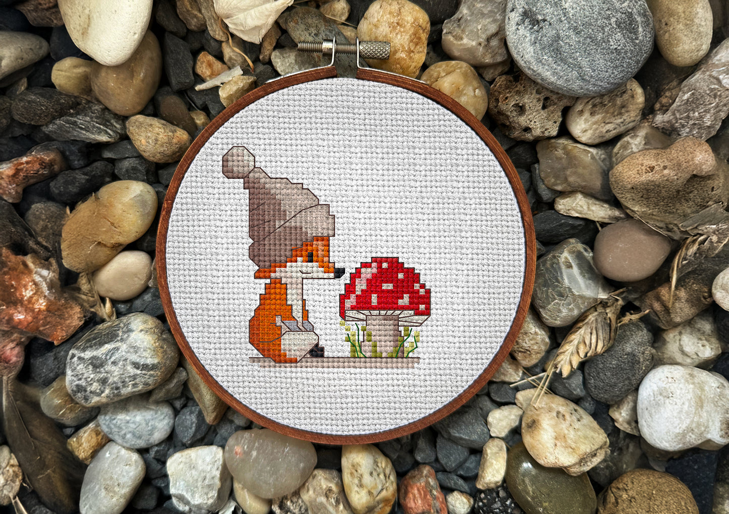 Cross stitch hoop with a little fox in a hat looking at a red mushroom