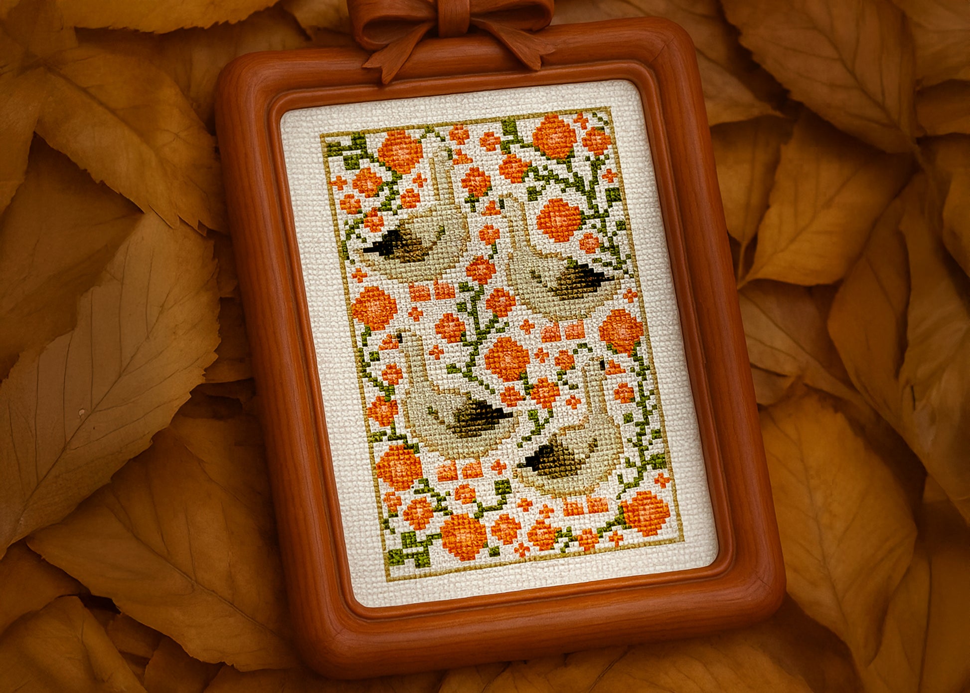 Framed cross-stitched piece with floral and bird pattern on a bed of autumn leaves.
