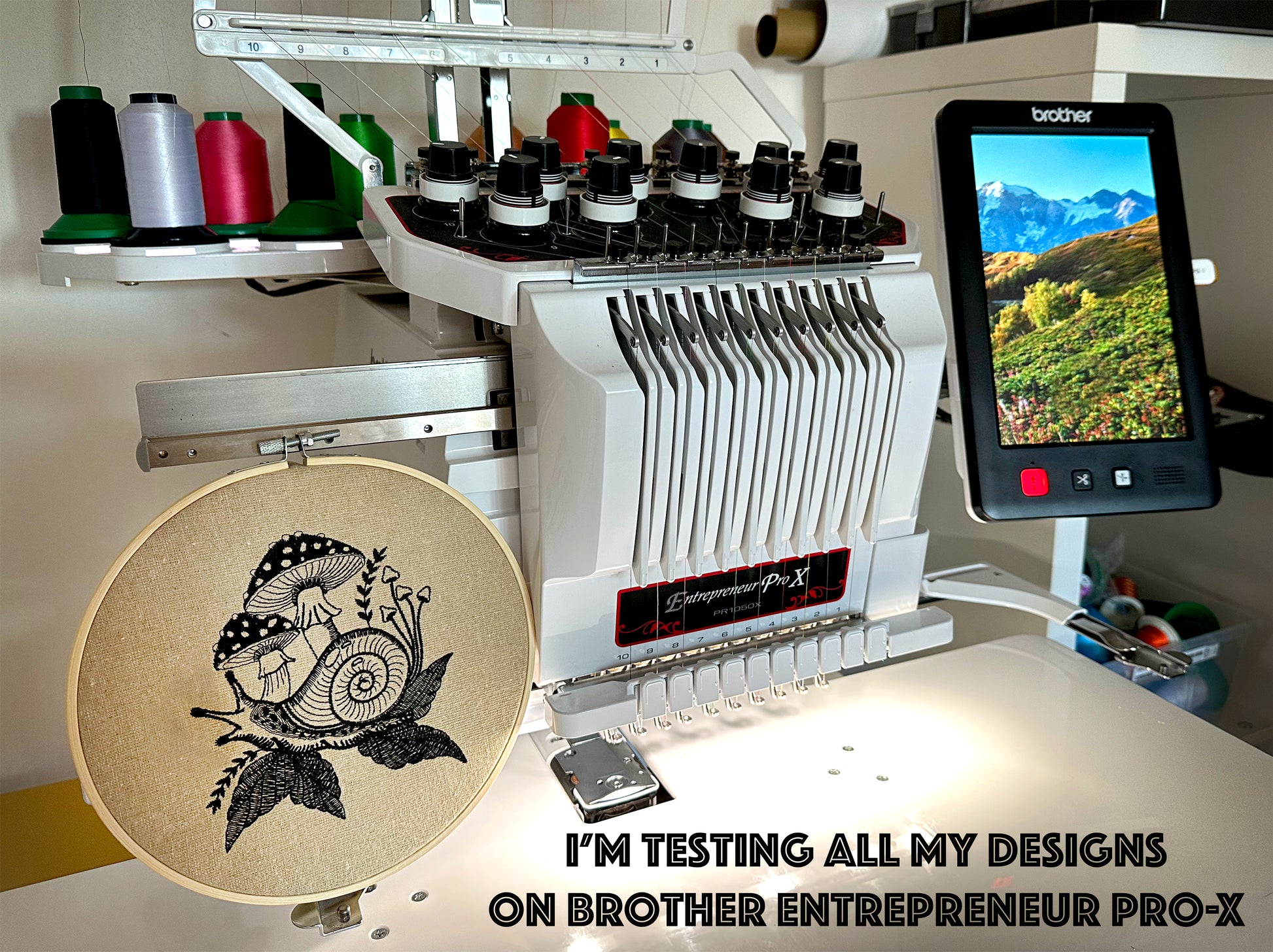 Embroidery machine with a screen displaying a mountain landscape and an embroidery hoop with a design.