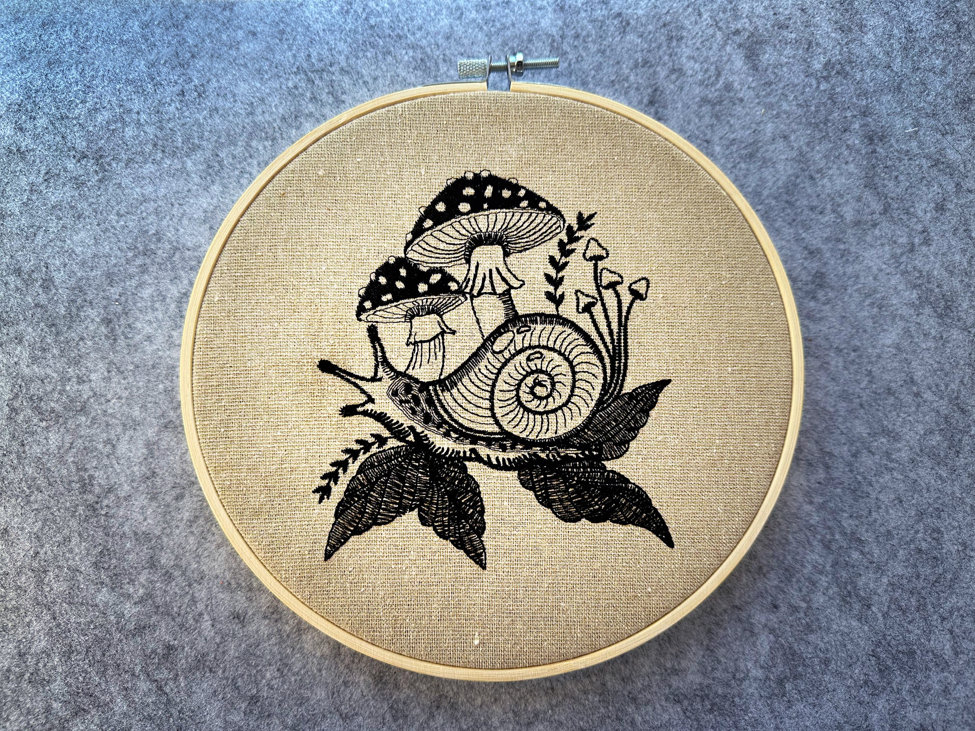 Snail and mushroom embroidery pattern stitched on linen in a hoop