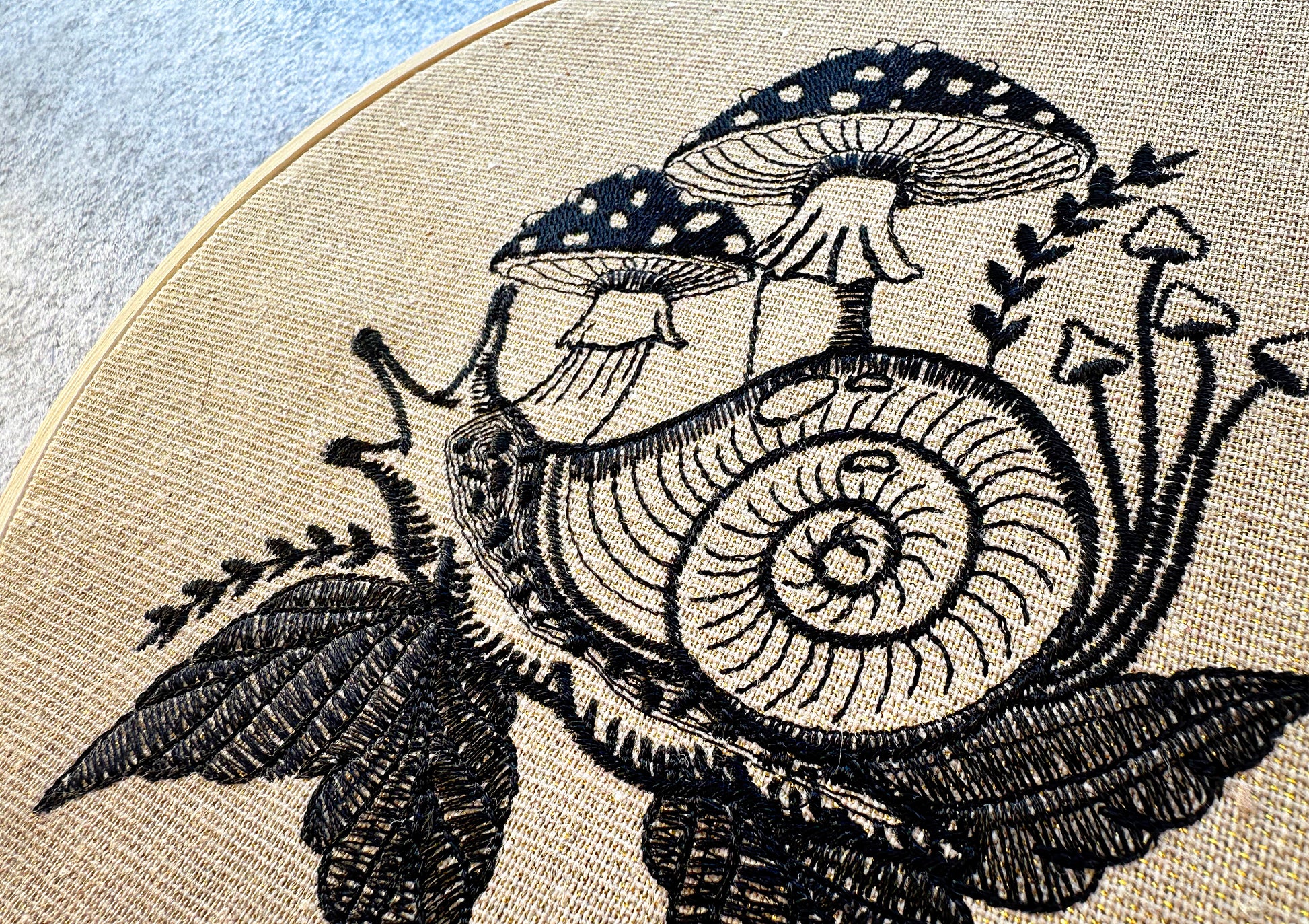 Monochrome embroidery design of a snail with toadstools and foliage