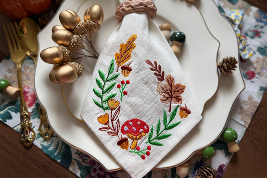 Decorative embroidered napkin on a plate with autumn-themed design, surrounded by decorative elements.