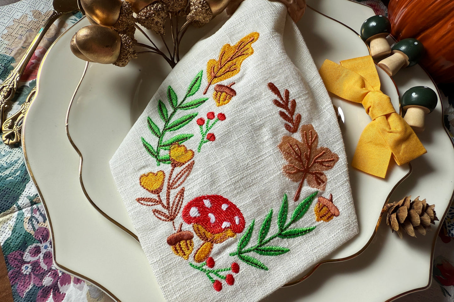 Embroidered towel with autumn-themed design on a decorative plate with fall decorations.