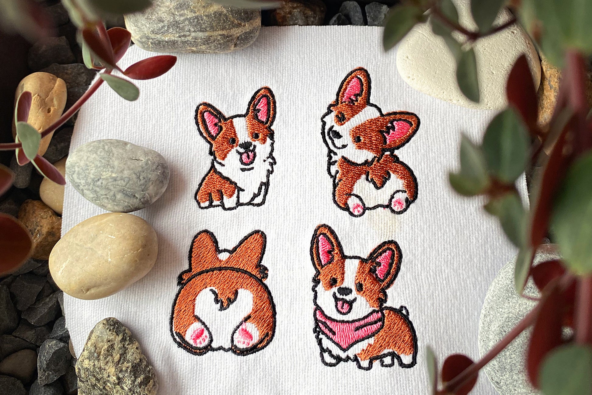 Embroidered corgi designs on a white fabric with rocks and plants in the background