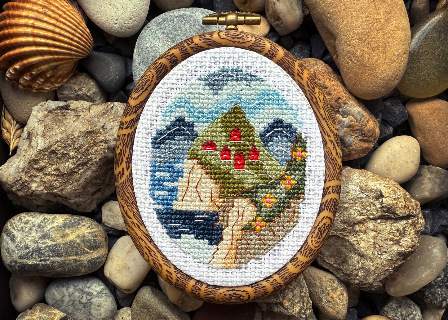 Cross-stitched piece of art in a wooden frame on pebbles