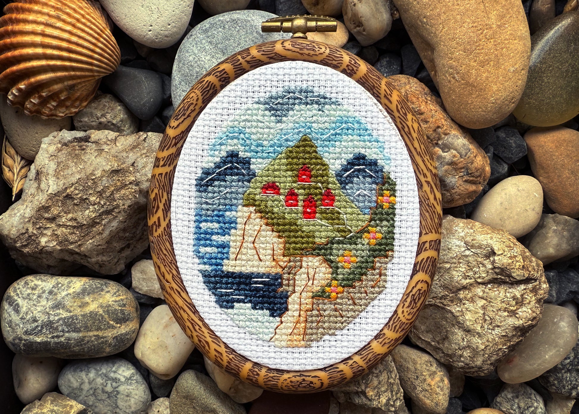 Cross-stitched piece of art in a wooden frame on pebbles