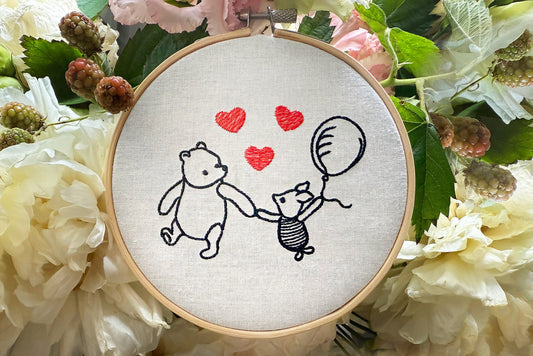 Finished Winnie and Piglet embroidery displayed in wooden hoop on soft brown background