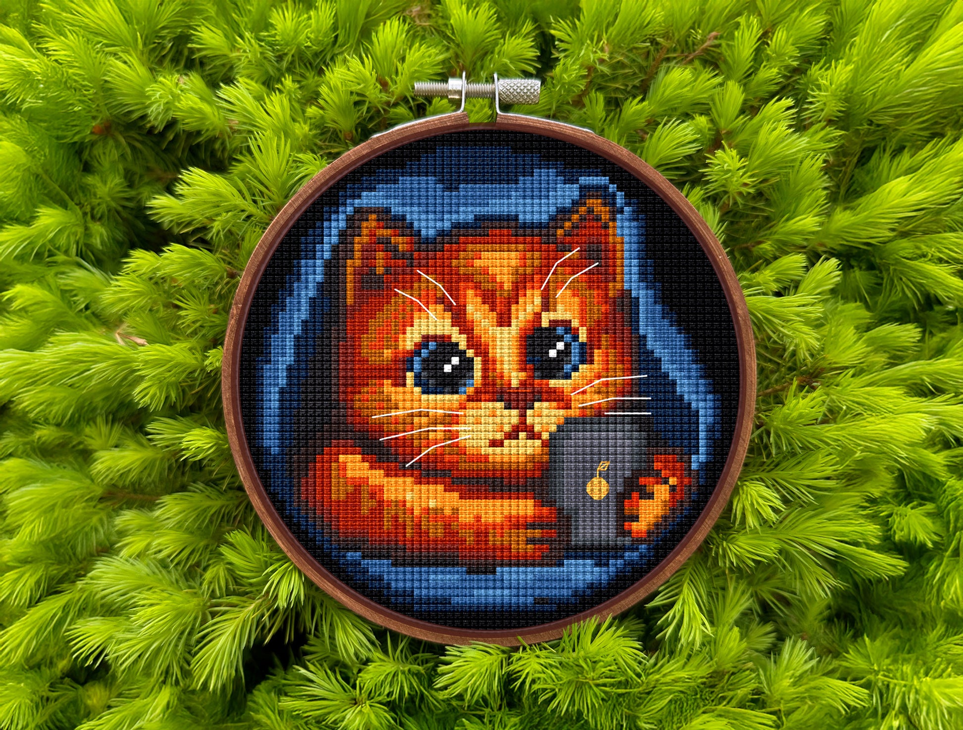 Cross-stitched cat design in an embroidery hoop on a green leafy background