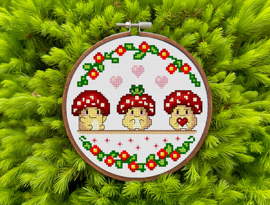 Embroidery hoop with mushroom-themed cross-stitch design on a green leaf background