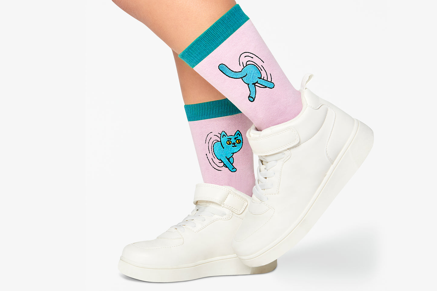 Pink socks with blue cat designs worn with white sneakers on a white background