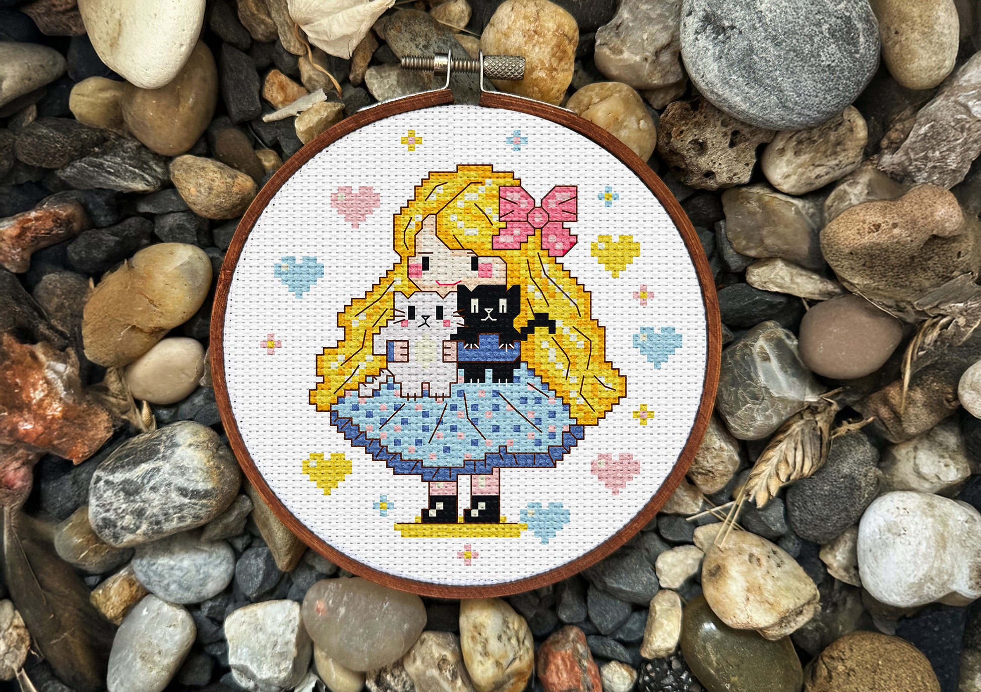 Cross-stitched design of a cartoon girl with a cat on pebbles